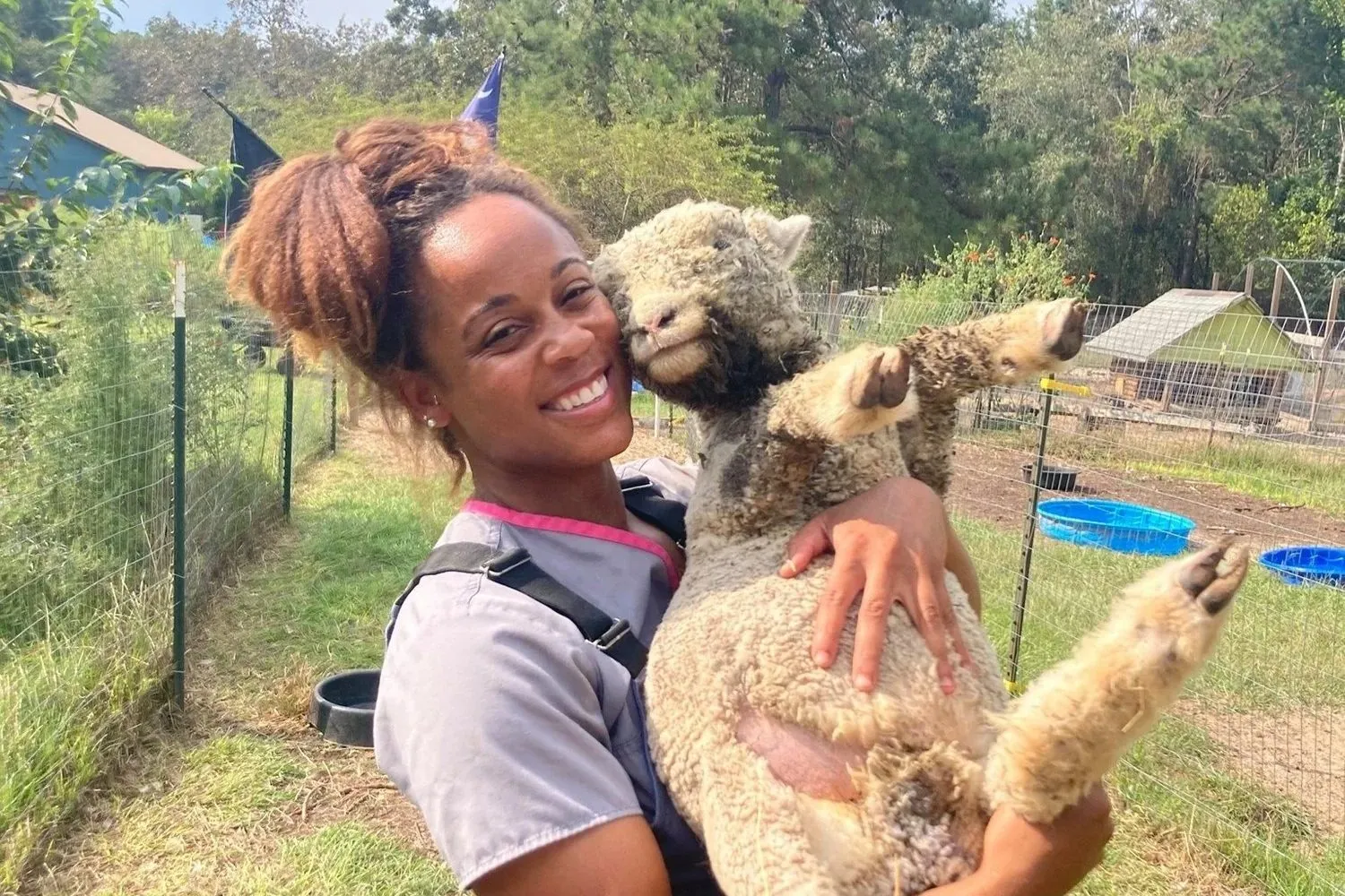 An Ark Veterinary Services vet smiling while holding an alpaca on a farm